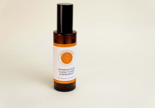 Bottle of frankincense, ylang ylang, and bergamot essential oil on a beige background