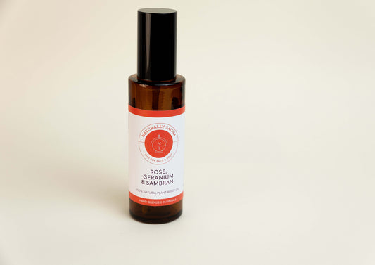 Bottle of rose, geranium, and sandalwood essential oil on a beige background