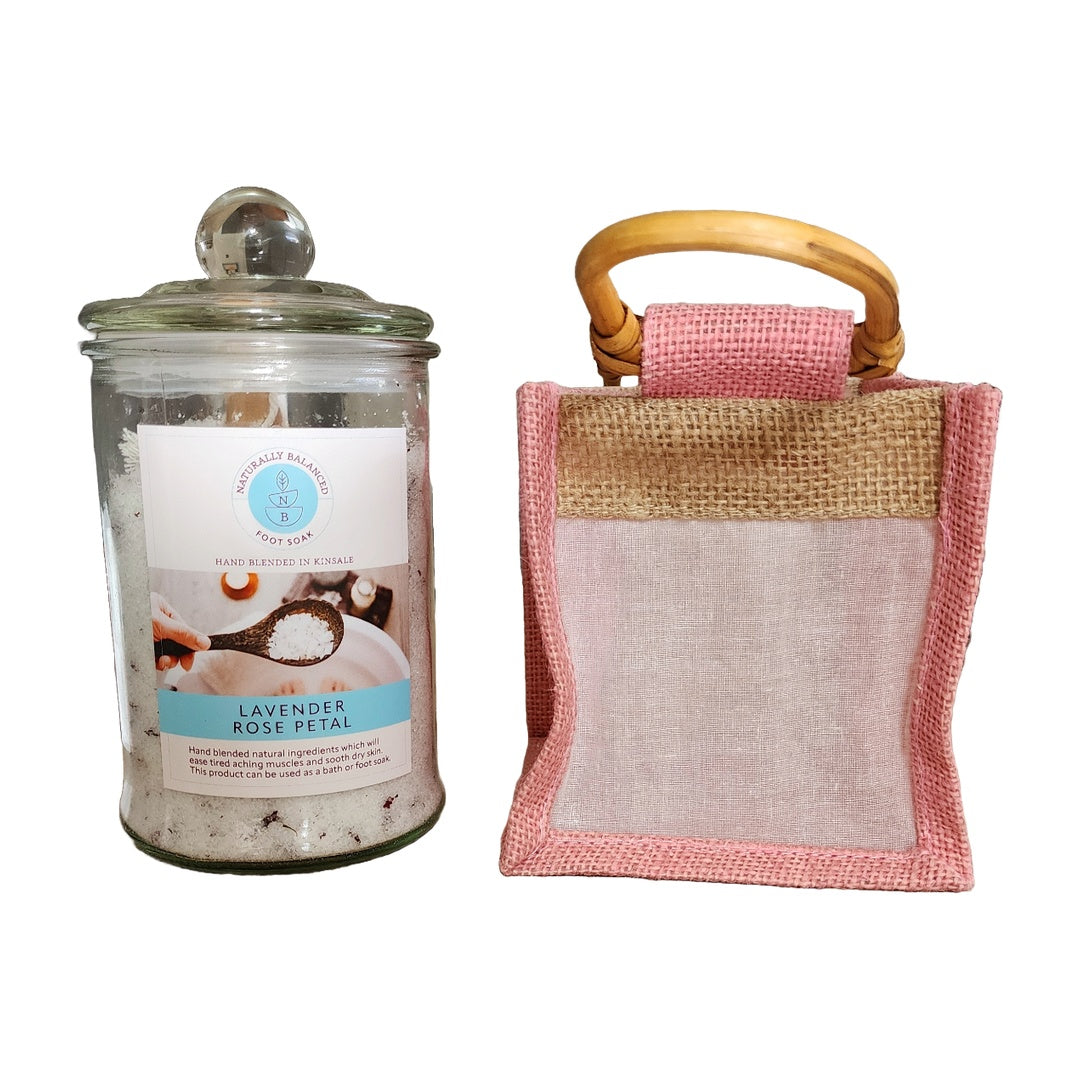 Glass jar with lavender rose petal bath salts and a pink loofah with wooden handle on a white background
