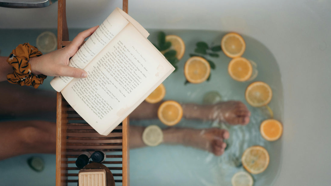 womans legs in a bath, reading with orange pieces in the water