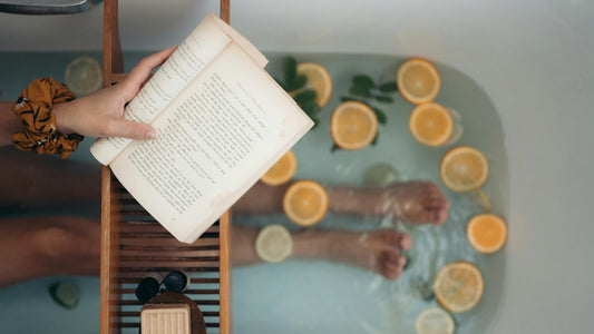 womans legs in a bath, reading with orange pieces in the water