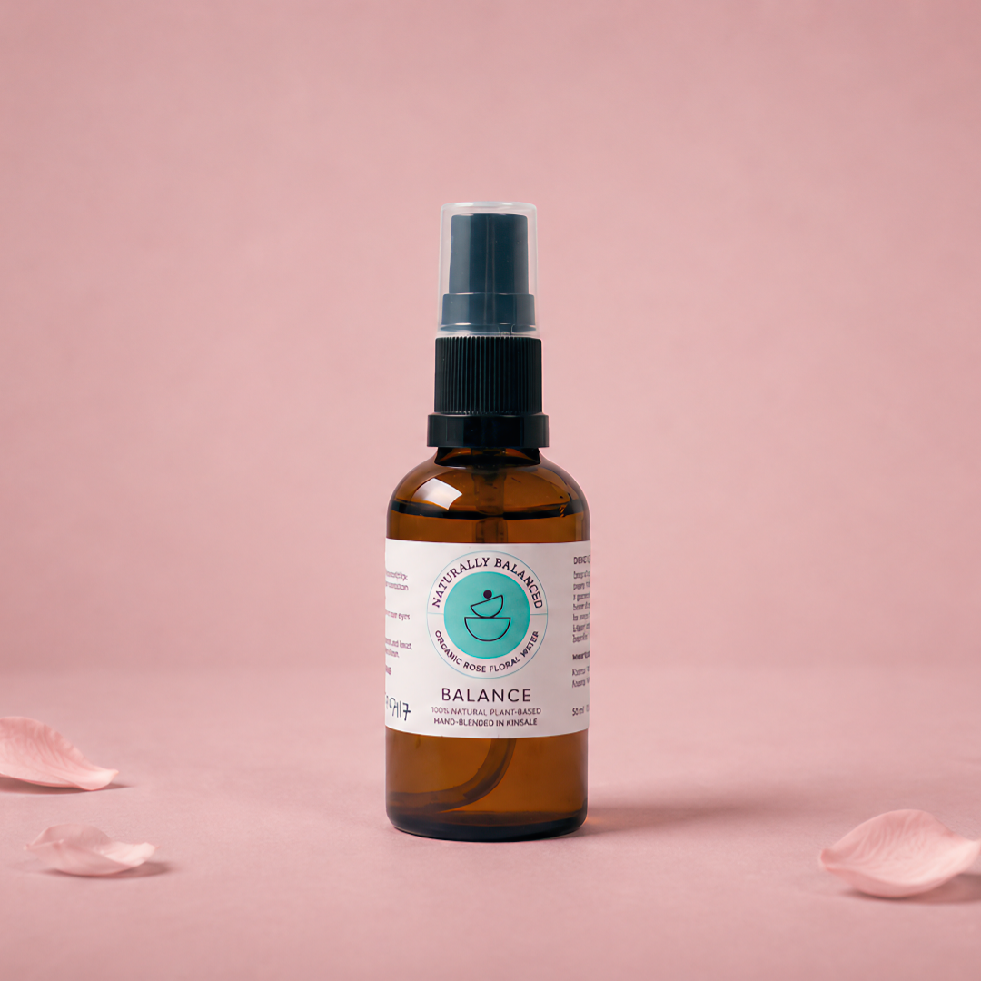 Bottle of 'Balance' spray with a label on a pink background with scattered rose petals.