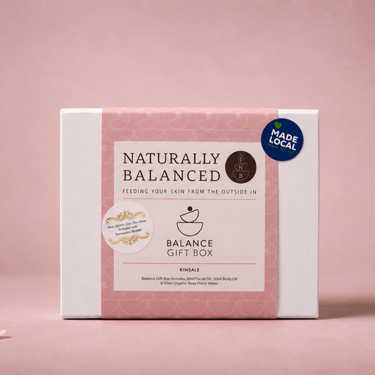 Gift box labeled 'Naturally Balanced' on a pink background with scattered petals.