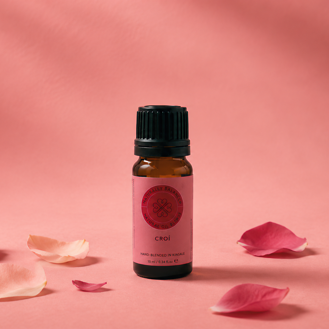 Small bottle of essential oil with pink flower petals on a pink background