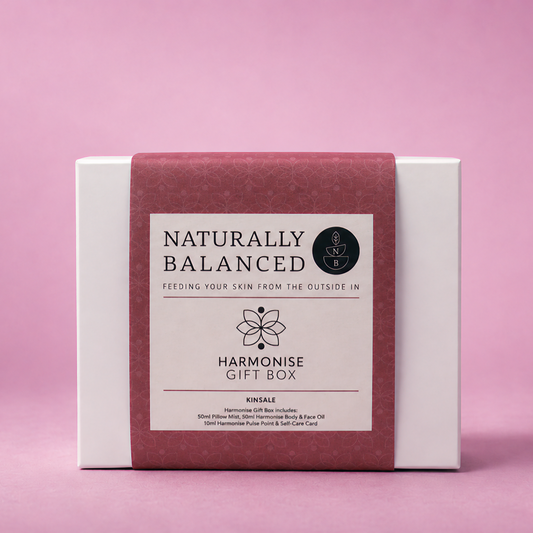 Gift box labeled 'Naturally Balanced' on a pink background with scattered petals.
