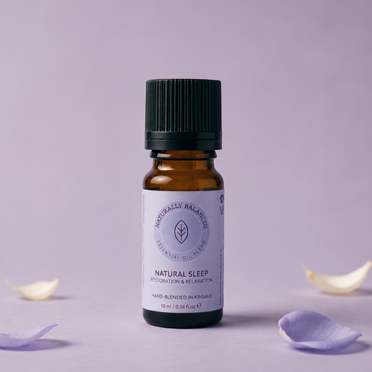 Bottle of 'Natural Sleep' essential oil with flower petals on a light purple background
