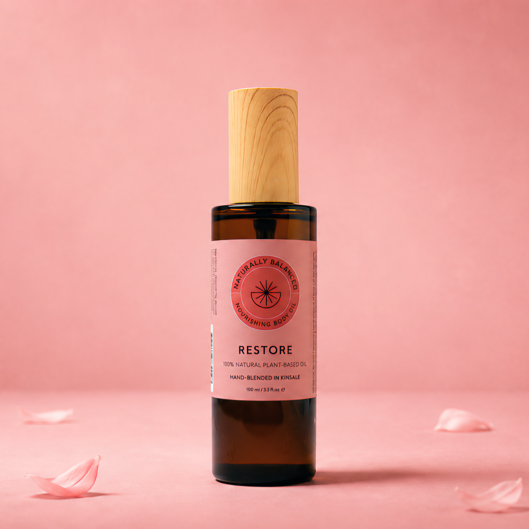 Bottle of 'Restore' oil with a wooden cap on a pink background with scattered rose petals.