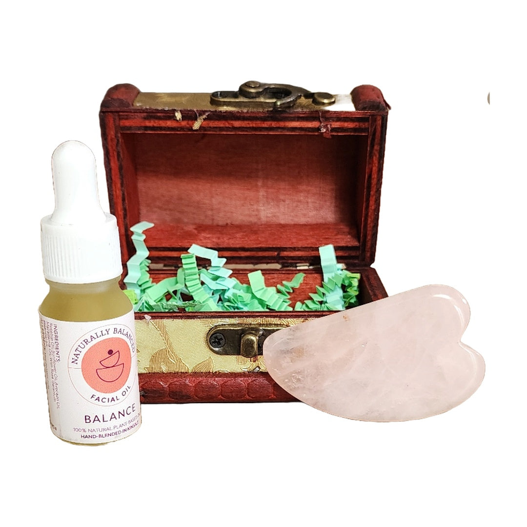 Facial oil bottle, gua sha tool, and open treasure chest on a white background